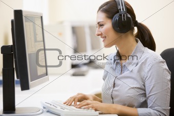 Woman wearing headphones in computer room typing and smiling