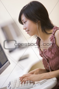 Woman in computer room listening to MP3 player while typing and 