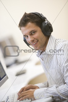 Man wearing headphones in computer room typing and smiling