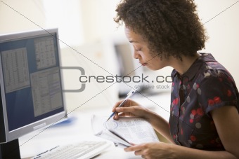 Woman in computer roon circling items in newspaper