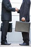 Two businessmen holding briefcases outdoors shaking hands