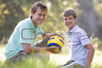 Man and young boy outdoors with soccer ball smiling