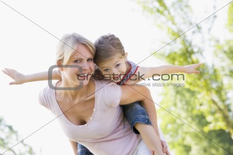 Woman giving young girl piggyback ride outdoors smiling