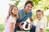 Man and two young children outdoors holding volleyball and smili