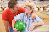 Man and young boy in bowling alley holding ball and smiling