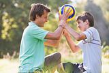 Man and young boy outdoors holding soccer ball and smiling