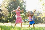 Woman and young girl outdoors using hula hoops and smiling