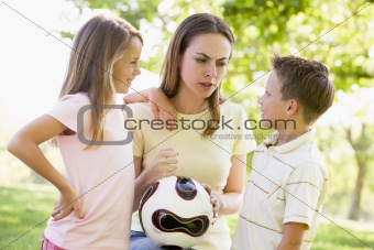 Woman and two young children outdoors holding volleyball and smi