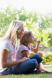 Woman and young girl outdoors blowing bubbles smiling