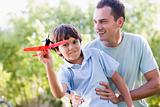 Man and young boy outdoors playing with toy airplane smiling