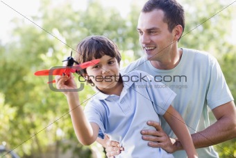 Man and young boy outdoors playing with toy airplane smiling