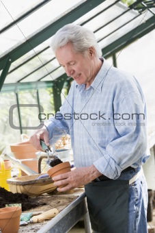 Man in greenhouse putting soil in pot smiling