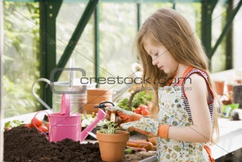 Young girl in greenhouse putting plant in pot