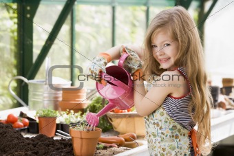 Young girl in greenhouse watering potted plant smiling