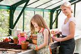 Young girl and woman in greenhouse putting soil in pots smiling