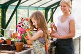 Young girl in greenhouse watering plant with woman holding pot s