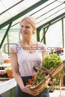 Woman in greenhouse holding basket of vegetables smiling