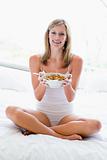 Woman sitting on bed eating cereal smiling