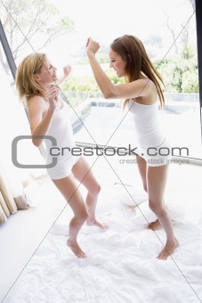 Two women jumping on bed smiling