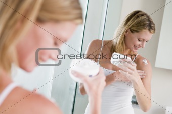 Woman in bathroom applying lotion smiling