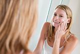 Woman in bathroom applying face cream smiling