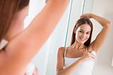 Woman in bathroom applying deodorant and smiling