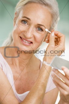 Woman applying eye makeup and smiling