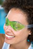 Woman sitting poolside using eye mask smiling