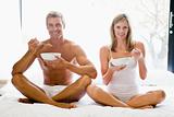 Couple sitting in bed eating cereal and smiling