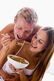 Couple sitting in bedroom eating cereal and smiling