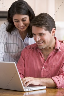 Couple in kitchen with paperwork using laptop smiling