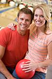 Couple in bowling alley holding ball and smiling