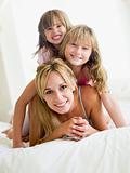 Woman and two young girls in bed playing and smiling
