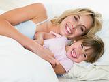 Woman and young girl in bed smiling