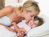 Woman kissing young girl in bed smiling