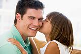 Young girl kissing smiling man in living room