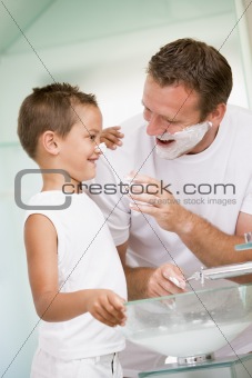 Man in bathroom putting shaving cream on young boy's nose