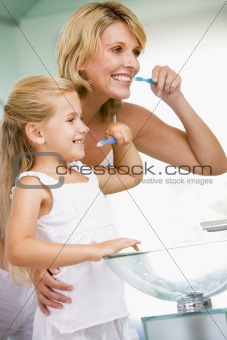 Woman and young girl in bathroom brushing teeth