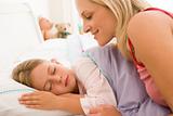 Woman waking young girl in bed smiling