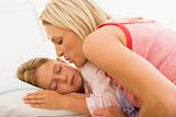 Woman waking young girl in bed with a kiss