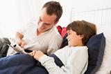 Man reading book to young boy in bed smiling
