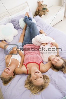 Woman lying in bed with two young girls laughing