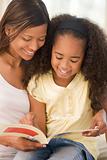 Woman and young girl sitting in living room reading book and smi