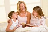 Woman with two young children sitting in bed reading book and sm