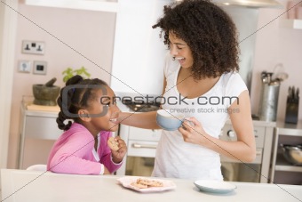 Woman and young girl in kitchen with cookies and coffee smiling