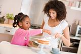 Woman and young girl in kitchen icing a cake smiling
