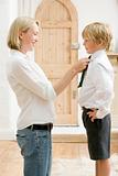 Woman in front hallway fixing young boy's tie and smiling