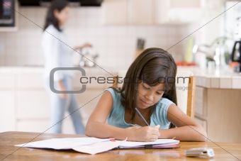 Young girl in kitchen doing homework with woman in background