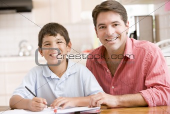 Man helping young boy in kitchen doing homework and smiling