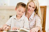 Woman and young boy reading book in dining room smiling